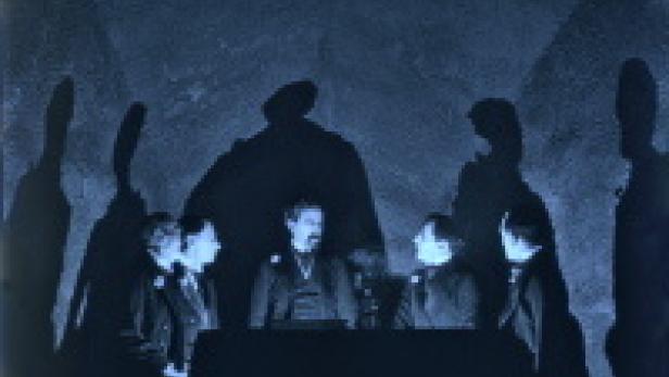 Eine Gruppe von Personen sitzt an einem Tisch, während Schatten an die Wand geworfen werden.