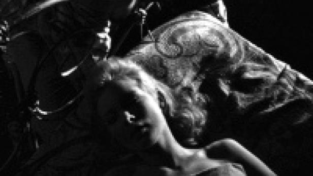 Eine junge Frau liegt in einem dunklen Raum auf einem verzierten Bett.