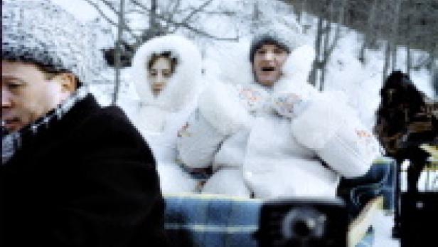 Ein Paar in dicken Winteranzügen sitzt in einem Schlitten im Schnee.