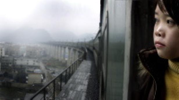 Ein Kind blickt aus dem Fenster eines Zuges auf eine Landschaft mit Bergen und einer Stadt.