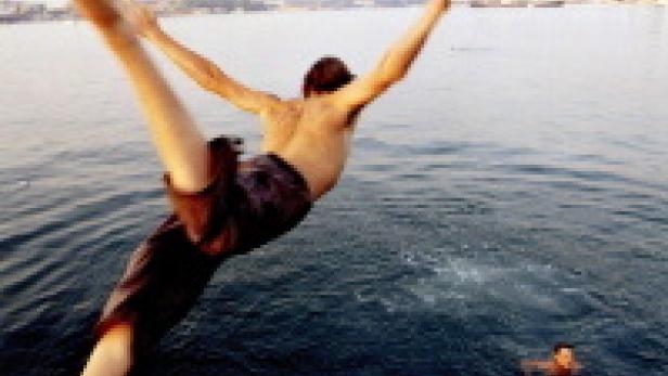 Ein Mann springt mit ausgestreckten Armen und Beinen ins Wasser.