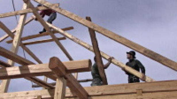 Mehrere Zimmerleute errichten ein Holzgebäude.