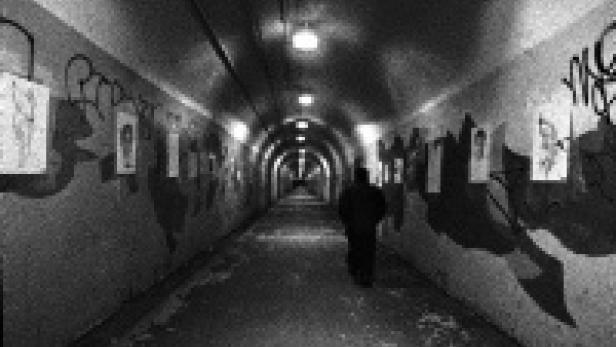 Eine Person geht durch einen langen, mit Graffiti und Bildern geschmückten Tunnel.
