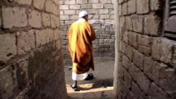 Ein Mann in orangefarbener Kleidung geht durch eine enge Gasse.