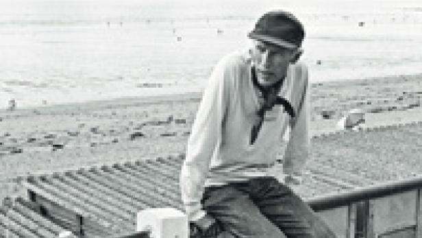 Ein Mann mit Mütze sitzt auf einer Mauer vor einer weiten Landschaft.