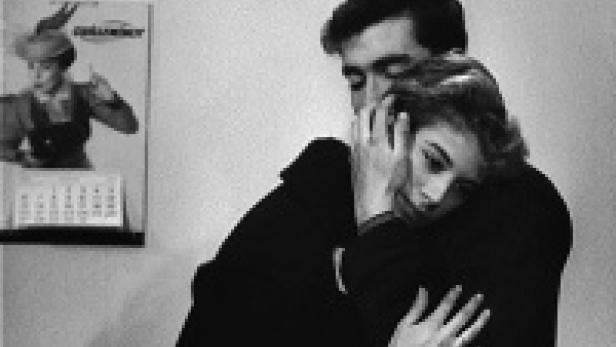 Ein Mann und eine Frau umarmen sich innig vor einem Kalender an der Wand.