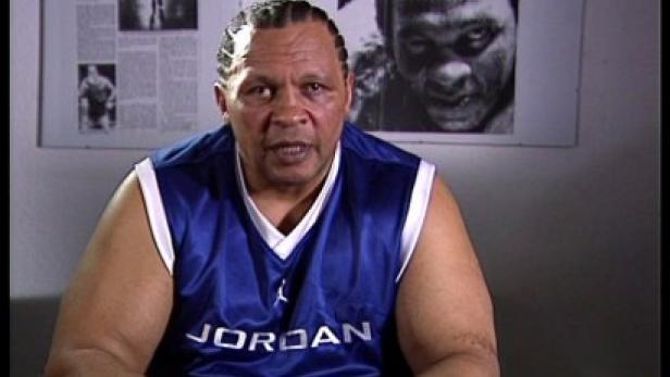 Ein Mann mit geflochtenem Haar trägt ein blaues Jordan-Trikot.