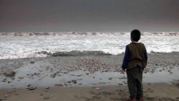 Ein Junge steht am Strand und blickt auf das Meer.