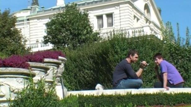 Zwei Personen sitzen vor einem Gebäude in einem Park.