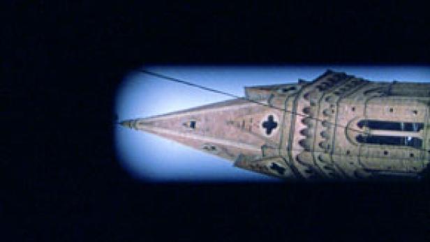 Detailaufnahme der Spitze eines Kirchturms vor blauem Himmel.