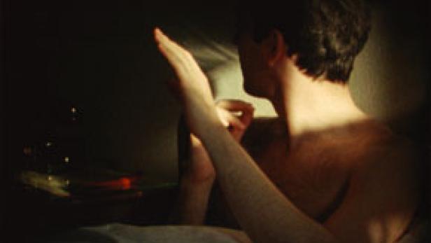 Ein Mann sitzt im Bett und hält eine Hand ins Licht.
