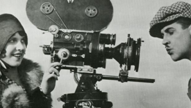 Eine Frau und ein Mann stehen neben einer alten Filmkamera.