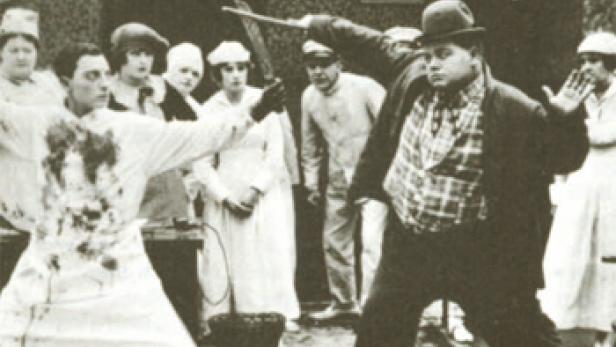 Szene mit Roscoe „Fatty“ Arbuckle, der in einem Film mit einem Kochmesser bedroht wird.