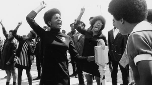 Eine Gruppe afroamerikanischer Demonstranten mit erhobenen Fäusten und lauten Rufen.