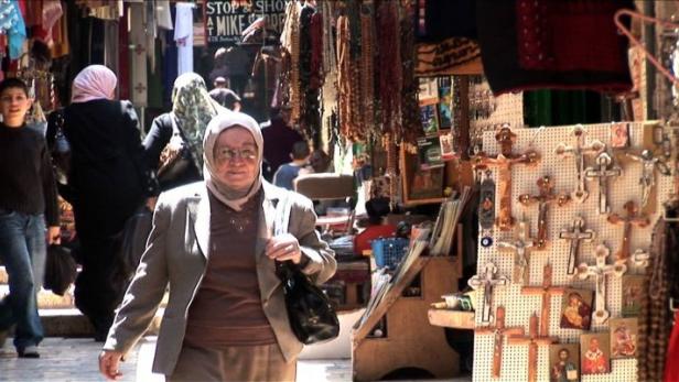 Eine Frau mit Kopftuch geht durch eine Gasse mit Verkaufsständen.