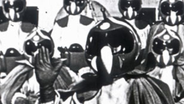 Eine Gruppe von Personen trägt futuristische Helme und Umhänge.