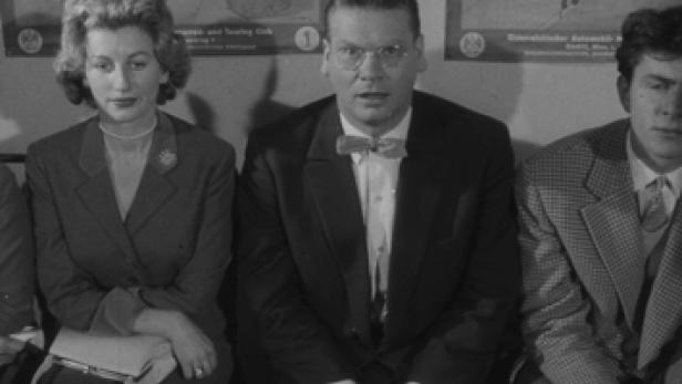 Eine Frau und zwei Männer sitzen nebeneinander in einem Wartebereich.