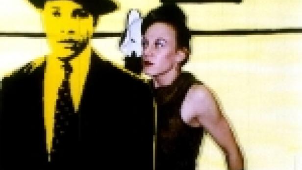 Ein Mann mit Hut und Anzug steht neben einer Frau in einem dunklen Kleid.