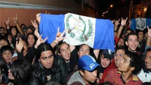 Eine Menschenmenge hält eine guatemaltekische Flagge hoch und jubelt.