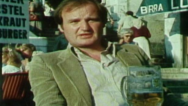 Ein Mann sitzt an einem Tisch im Freien mit einem Bierglas vor sich.