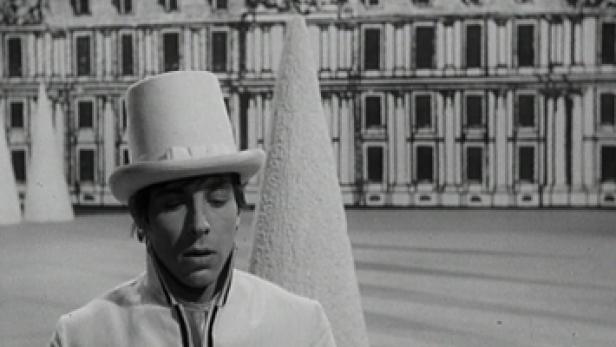 Ein Mann mit Zylinder und weißem Anzug vor einem gemalten Schloss.