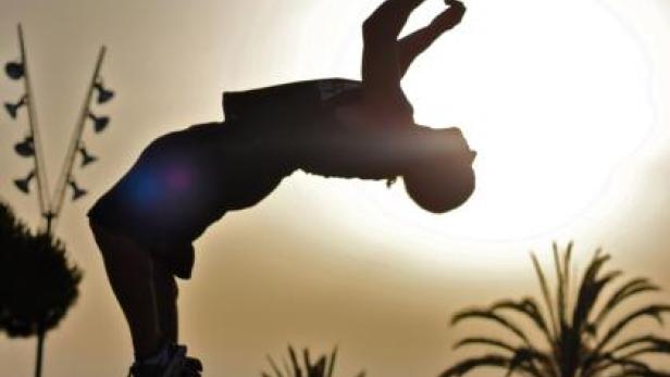 Die Silhouette eines Mannes, der vor dem Hintergrund der untergehenden Sonne einen Rückwärtssalto macht.