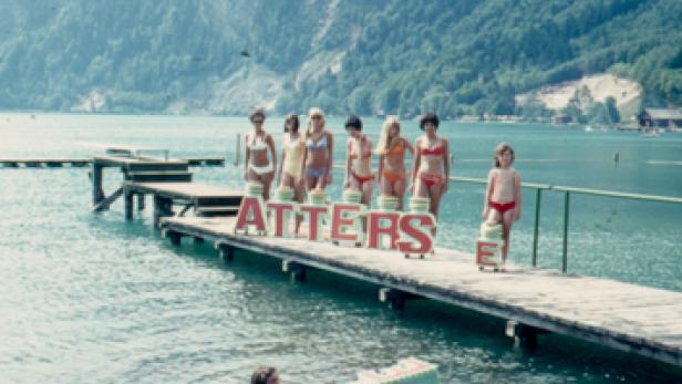 Eine Gruppe junger Frauen posiert mit dem Schriftzug „Attersee“ auf einem Steg im Wasser.