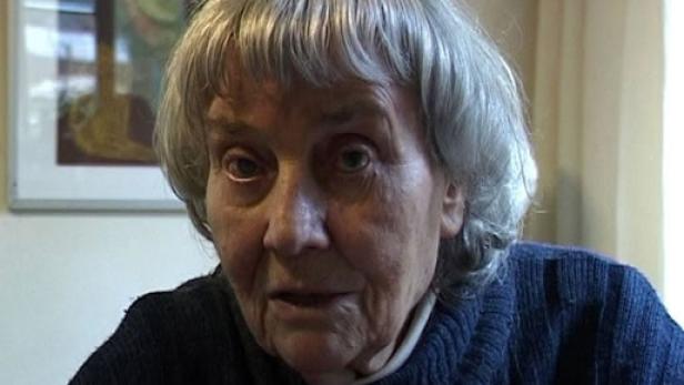 Eine ältere Frau mit grauen Haaren schaut in die Kamera.