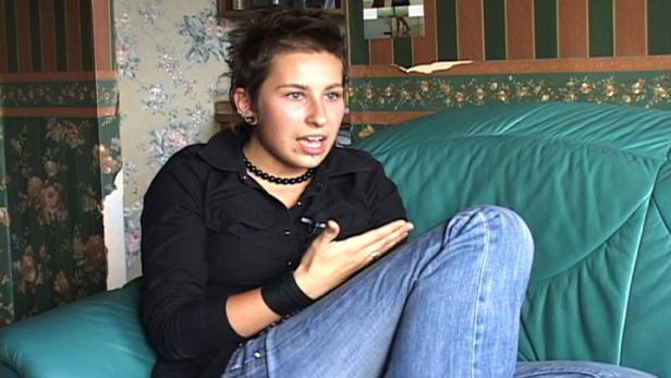 Eine junge Frau mit kurzen Haaren sitzt auf einem grünen Sofa und gestikuliert.