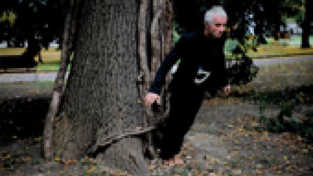 Ein Mann in schwarzer Kleidung lehnt an einem Baum in einem Park.