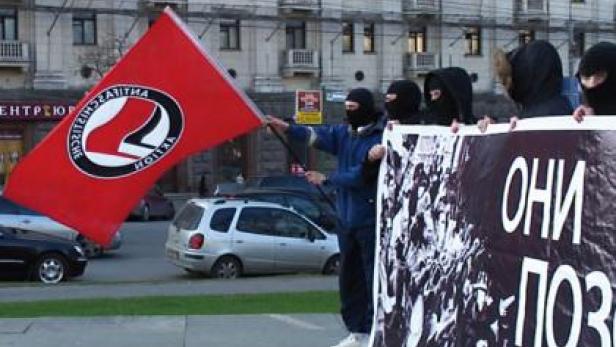 Vermummte Personen demonstrieren mit einer Antifa-Fahne und einem Banner.