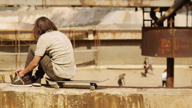 Ein junger Mann sitzt auf einem Skateboard und bindet seine Schuhe.
