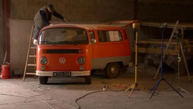 Eine orangefarbene VW-Kastenwagen wird in einer Werkstatt restauriert.