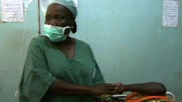 Eine Krankenschwester in OP-Kleidung hält die Hand eines Patienten.