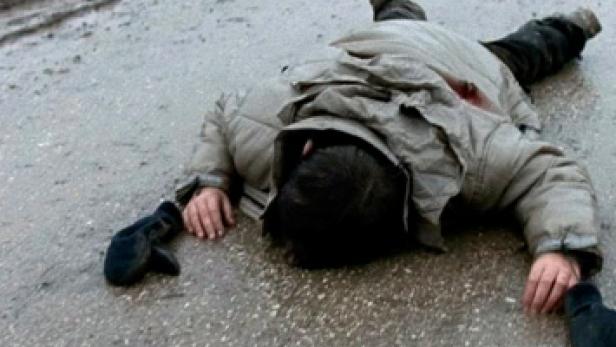 Eine Person liegt leblos auf einer nassen Straße.