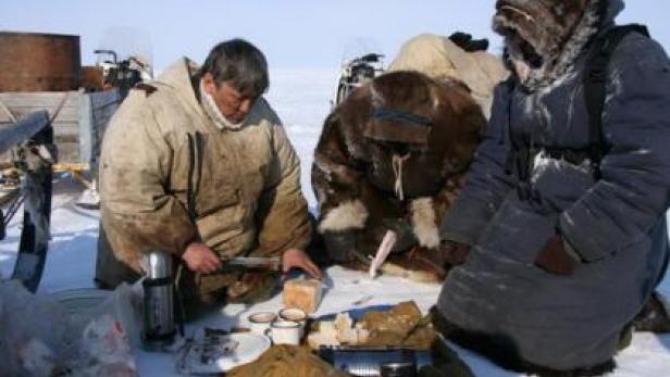 Eine Gruppe von Menschen macht im Schnee eine Pause und isst Brot.