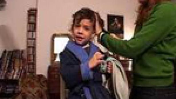 Ein Kind im Bademantel sitzt, während eine Frau seine Haare kämmt.