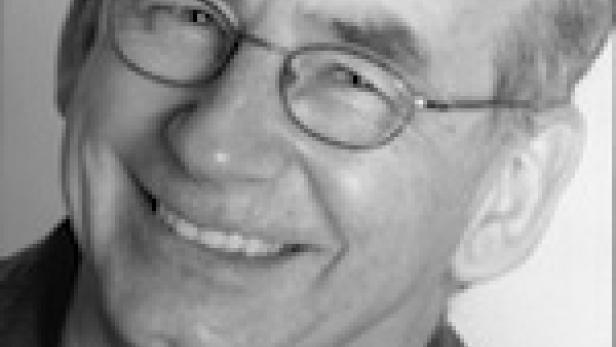 Ein lächelnder Mann mit Brille in Schwarzweiß.