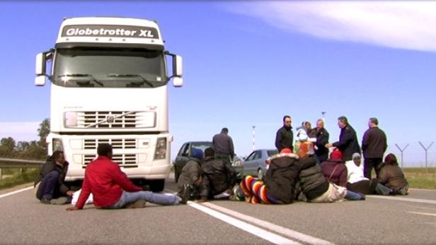 Eine Gruppe von Menschen blockiert eine Straße mit einem LKW.