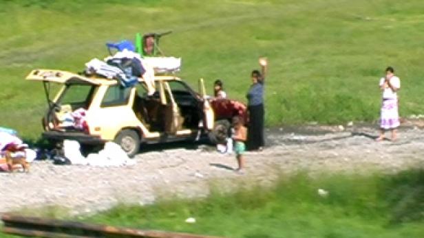 Eine Familie steht neben einem vollgepackten Auto am Straßenrand.