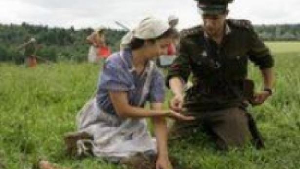 Eine Frau im Kleid und ein Soldat knien auf einem Feld.