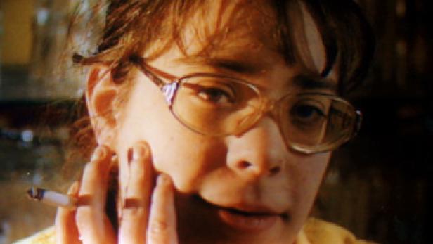 Eine Frau mit Brille hält eine Zigarette in der Hand.