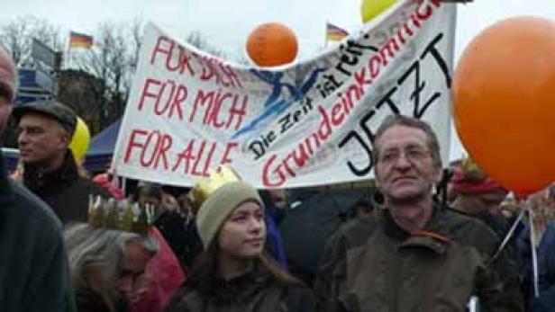 Menschen demonstrieren für ein Grundeinkommen, mit einem Banner „Für dich, für mich, für alle“.