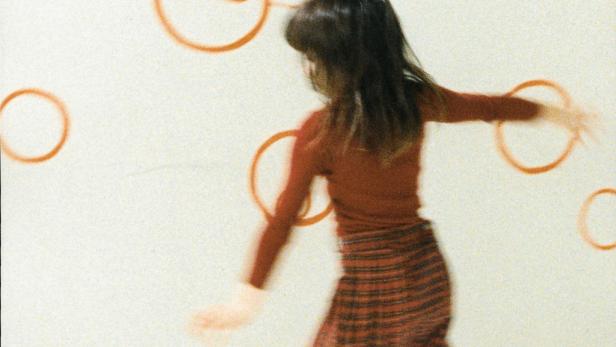 Ein Mädchen tanzt vor einer Wand mit orangefarbenen Kreisen.
