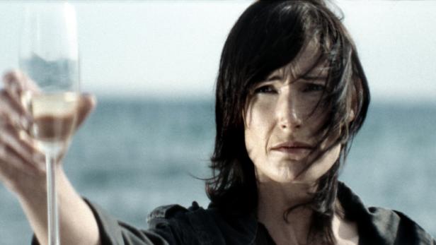 Eine Frau hält ein Glas Sekt vor dem Hintergrund des Meeres.