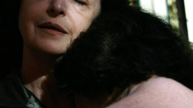 Eine ältere Frau umarmt ein Kind mit dunklen Haaren.