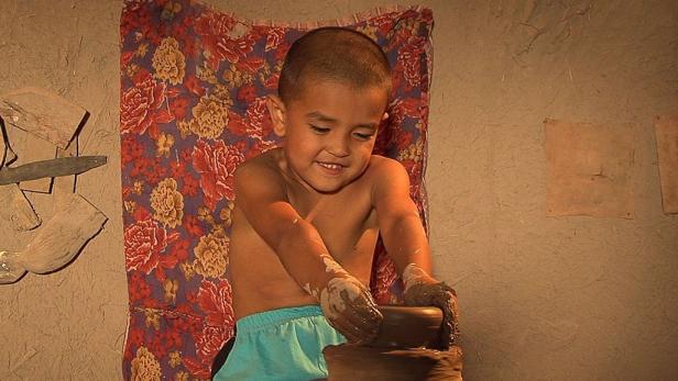 Ein Junge formt mit schmutzigen Händen einen Tontopf.