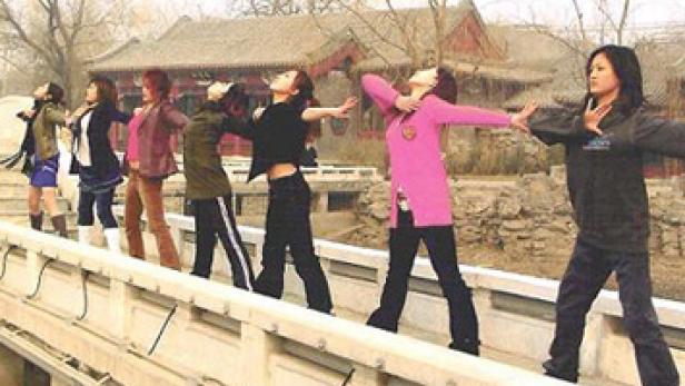 Eine Gruppe junger Frauen posiert auf einer Brücke mit einem traditionellen chinesischen Gebäude im Hintergrund.