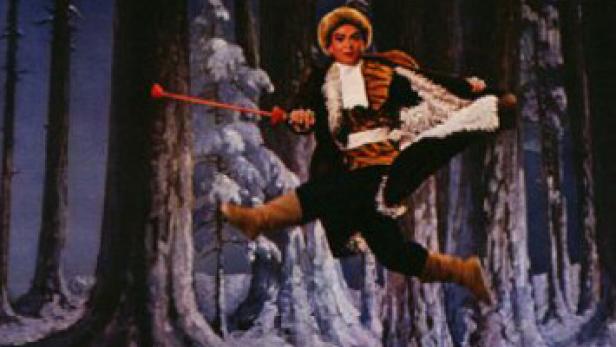 Ein Tänzer in einem Kostüm springt vor einem Bühnenbild mit verschneiten Bäumen.