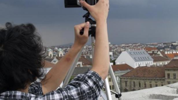 Eine Person fotografiert mit einem Stativ eine Stadtansicht unter einem bewölkten Himmel.